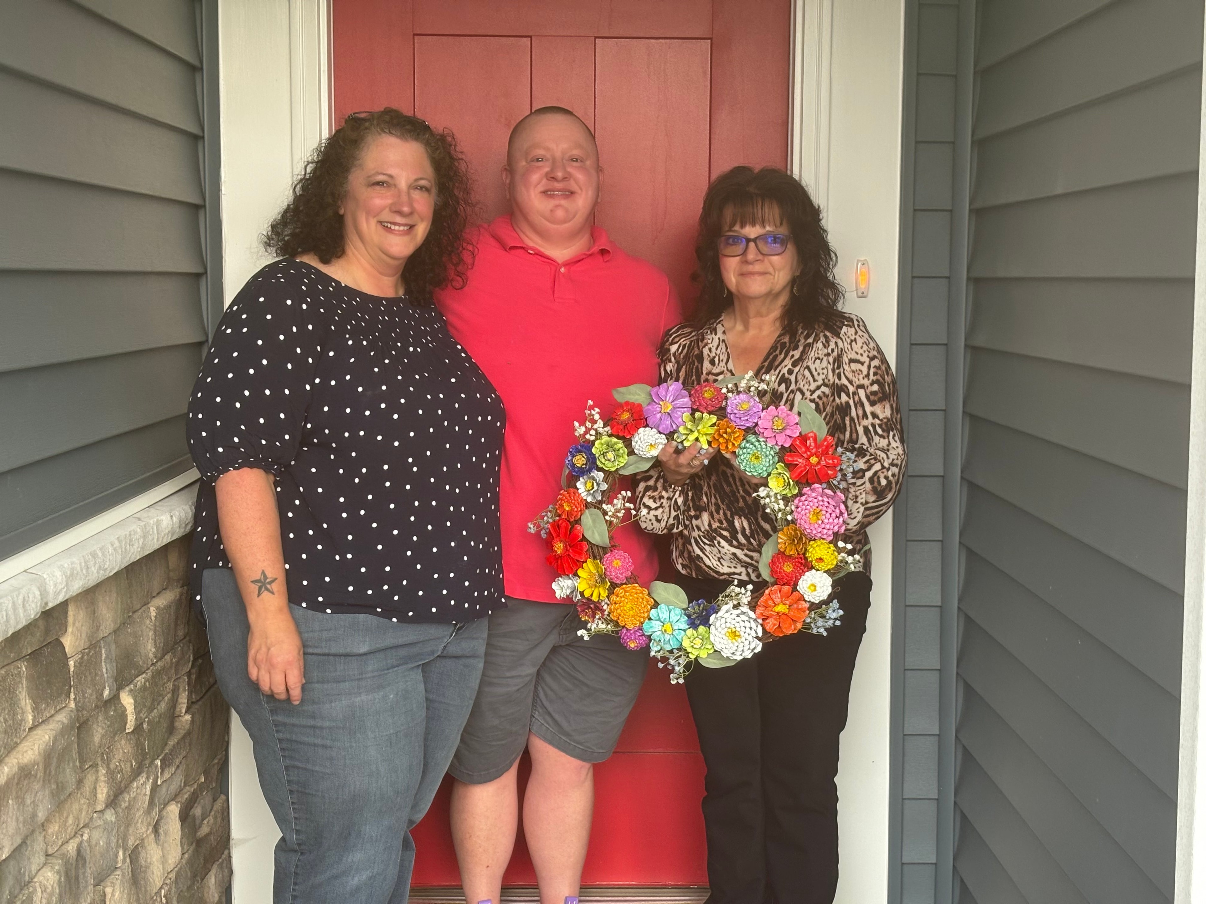 Agent and clients celebrating at the front door of their new home with a flower wreath