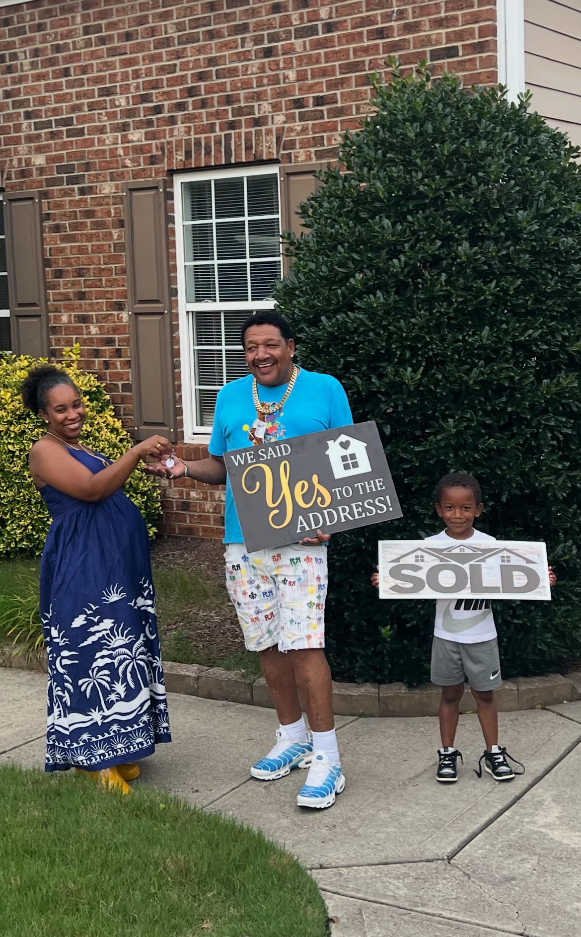 Family in front of brick home holding SOLD and Our New Home signs